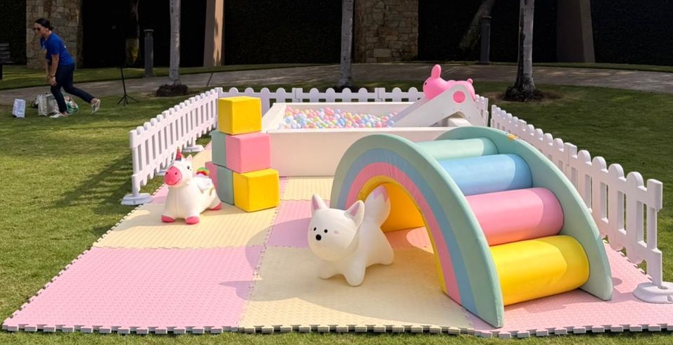 Zona soft-play premium con bloques de espuma, arcoíris, piscina de pelotas y vallado blanco para niños pequeños.